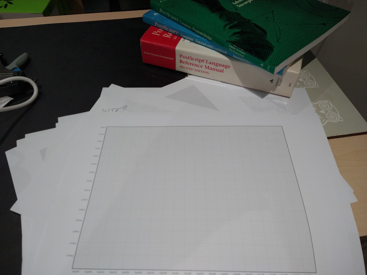 Gigatron graph paper on a pile of failed attempts. PostScript manuals in the background.